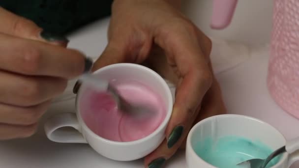 Una mujer hace glaseado de azúcar de color para decorar las galletas de jengibre. Mezcla esmalte con tinte rojo. Cerca de una taza con hielo verde . — Vídeos de Stock