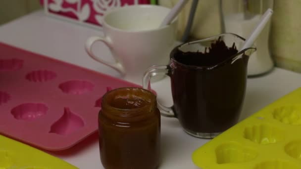 Mujer pone con un cepillo de chocolate líquido negro en forma de silicona. Para la preparación de dulces vidriados. Cerca se encuentran otros ingredientes de cocina . — Vídeos de Stock