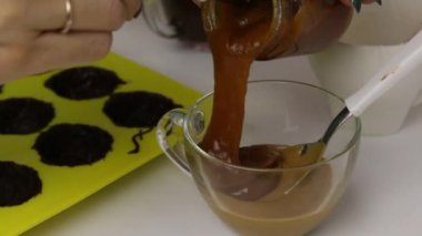 Kadın jöleli şekerleri karıştırıyor. Yakınlarda sıvı çikolatayla yağlanmış silikon bir küf var..
