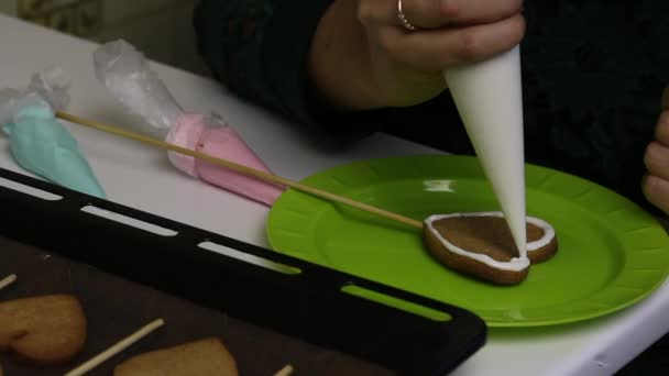 Une femme applique un glaçage au sucre blanc sur les biscuits au pain d'épice. A proximité sur une plaque à pâtisserie sont des cookies pour la décoration . — Video