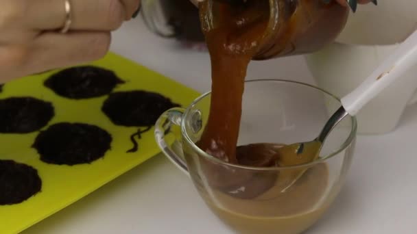 女人把加满了釉料的糖果混合在一起. 附近是一个用液体巧克力润滑的硅胶模具. — 图库视频影像