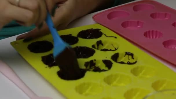 女性はブラシでシリコーンフォームに液体チョコレートを適用します。焼き菓子の準備のために. — ストック動画