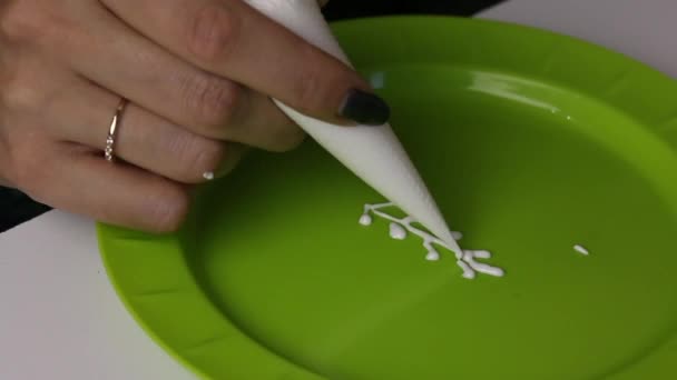 Een vrouw houdt in haar handen een banketbakje met witte suiker glazuur om gember koekjes te versieren. Controleert de kwaliteit van het glazuur, zet het op een bord. — Stockvideo