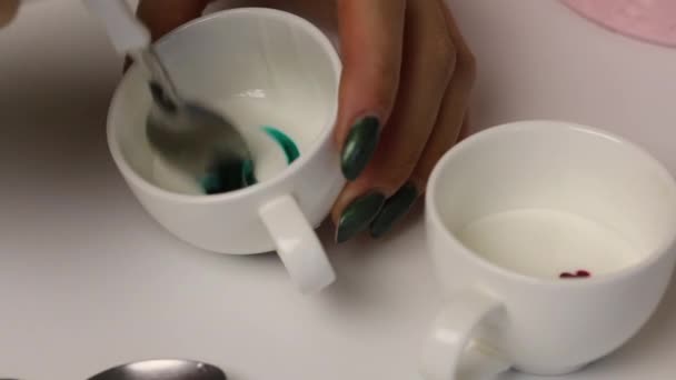 Een vrouw maakt gekleurde suiker glazuur om gember koekjes te versieren. Mengt het glazuur met de groene kleurstof. — Stockvideo