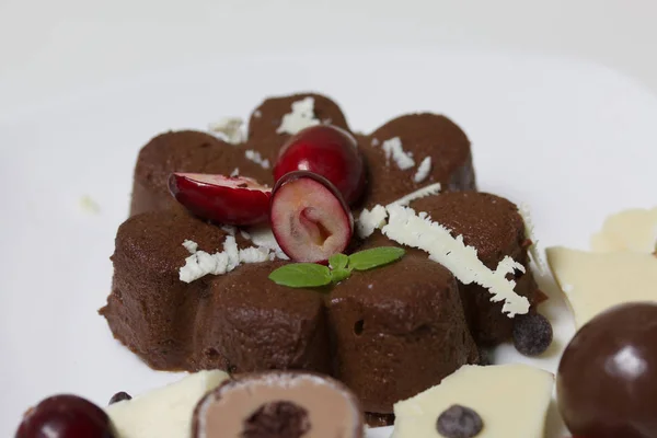Chokladkola garnerad med choklad, mynta och tranbär. Ligger på en vit platta, på en vit bakgrund. — Stockfoto