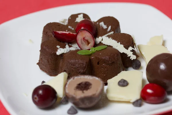 Chokladkola garnerad med choklad, mynta och tranbär. Ligger på en vit platta, på en korall bakgrund. — Stockfoto