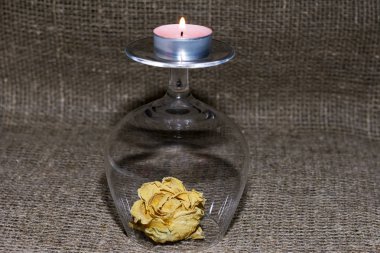 Kurumuş gül çiçeği. Şarap kadehiyle kaplanmış. Bardağın dibinde yanan bir mum var. Keten kumaş üzerinde.