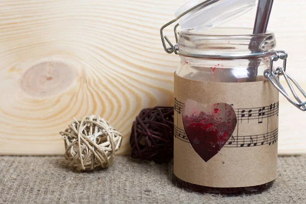 Glass jar of jam wrapped in paper with notes. Heart cut out in paper. Near rattan balls.