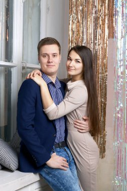 Genç bir adam karısına sarılıyor. Boynuna sarılıyor. Parlayan yağmur perdesinin yanında.