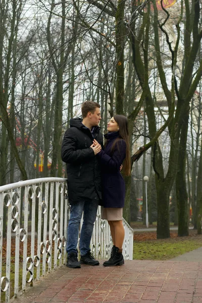 Giovane coppia posa vicino alla ringhiera di un ponte pedonale nel parco. Fine autunno, nebbia . — Foto Stock