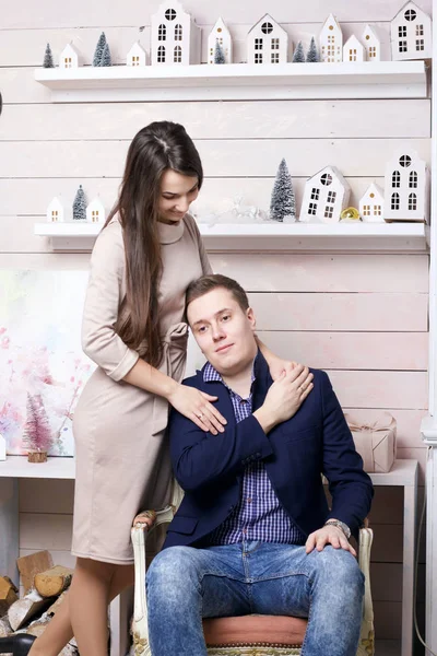 Ένας νεαρός κάθεται σε μια καρέκλα και κρατά τη γυναίκα του από το χέρι. Μια σύζυγος στέκεται κοντά και αγκαλιάζει το λαιμό του. — Φωτογραφία Αρχείου