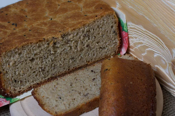Nybakat bröd. Skivor bröd skärs och ligger bredvid dem på en skärbräda. Ytan är täckt med linne. — Stockfoto