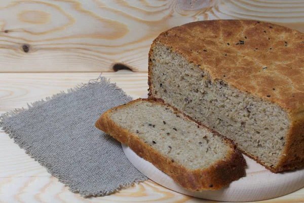 Свежеиспеченный хлеб. Кусок хлеба режется и лежит на разделочной доске. Рядом с куском льняной ткани. Фон из сосновых досок . — стоковое фото