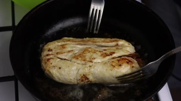 Em uma frigideira aquecida na manteiga, o rolo de filé de frango é frito. Um homem vira o rolo com garfos. Você pode ver como o óleo ferve e uma crosta dourada aparece . — Vídeo de Stock