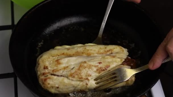 In a heated frying pan in butter, the chicken fillet roll is fried. A man holds a roll with forks. You can see how the oil boils and a golden crust appears. — Stockvideo