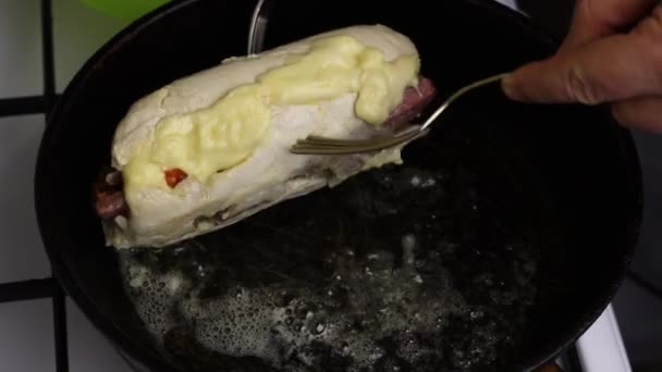 In una padella riscaldata nel burro, il rotolo di filetto di pollo viene fritto. Un uomo ribalta il rotolo con le forchette. Potete vedere come l'olio sta bollendo . — Video Stock