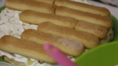 Bir kadın Savoiardi kurabiyelerinden kek yapıyor. Bir kadın krema ve ananas katmanına kurabiye koyar. Yakın çekim..