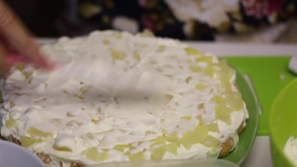 A woman makes a cake from Savoiardi cookies. Pineapples laid on a cream. The woman applies the next layer of cream. — Stock Video