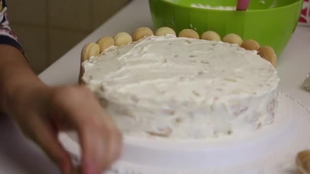 A woman decorates a cake of Savoiardi cookies. Slices cookies and puts it in a circle of cake. — Stock Video