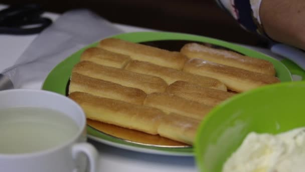 Eine Frau backt einen Kuchen aus savoiardi-Keksen. in Sirup tauchen und Kekse reihenweise auf ein Substrat legen. — Stockvideo