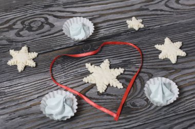 Şekerlemeler ve marşmelovlardan gelen kar taneleri. Yakınlarda kalp şeklinde yerleştirilmiş kırmızı bir kurdele var. Eski çam ağaçlarında siyaha boyanmış.