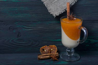 Cam kadehlerde iki kat jöle. Krema ve mandalina jölesi. Yakınlarda dekorasyon için baharatlar var. Fırçalanmış tahtaların yüzeyinde siyah ve yeşile boyanmış.