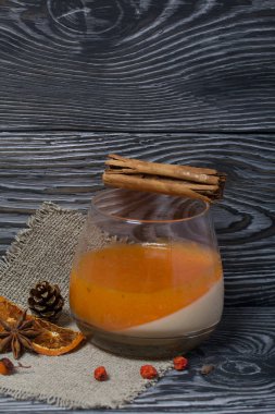 Cam kadehlerde iki kat jöle. Krema ve mandalina jölesi. Reçelli bardakta tarçın çubukları. Dekorasyon için baharatların yanında. Fırçalanmış tahtaların yüzeyinde siyah ve yeşile boyanmış.