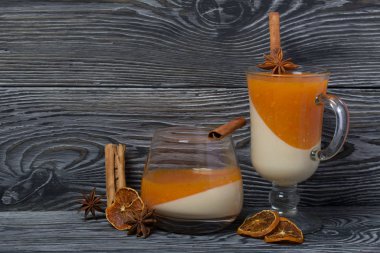 Cam kadehlerde iki kat jöle. Krema ve mandalina jölesi. Jöle, tarçın çubuğu ve anason. Dekorasyon için baharatların yanında. Fırçalanmış tahtaların yüzeyinde siyah ve yeşile boyanmış.