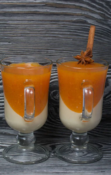 Two layers of jelly in glass goblets. Cream and tangerine jelly. In jelly, cinnamon stick and anise. On the surface of brushed boards painted in black and white.