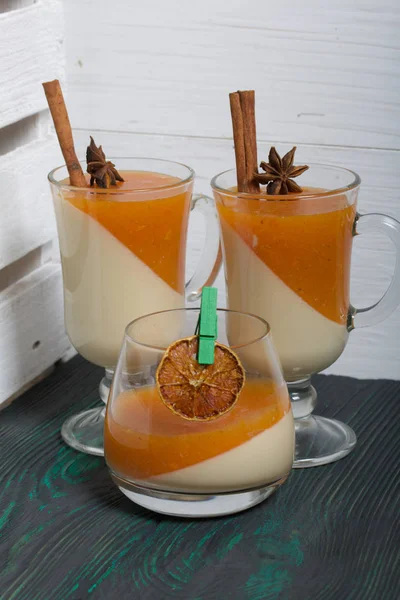 Two layers of jelly in glass goblets. Cream and tangerine jelly. In jelly, cinnamon stick and anise. On the surface of brushed boards painted black and green. — Stock Photo, Image