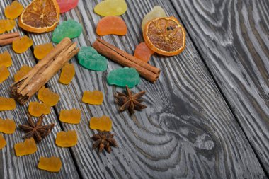 Jöle çiğneyen şekerler. Kurutulmuş portakal dilimleri, tarçın çubukları ve anason yıldızları. Fırçalanmış çam ağaçlarının üzerine siyah beyaz boyanmış..