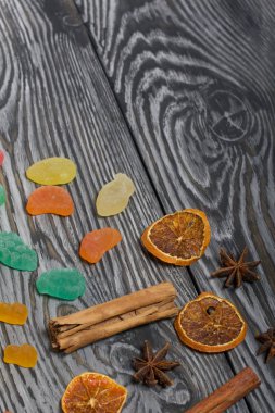 Jöle çiğneyen şekerler. Kurutulmuş portakal dilimleri, tarçın çubukları ve anason yıldızları. Fırçalanmış çam ağaçlarının üzerine siyah beyaz boyanmış..