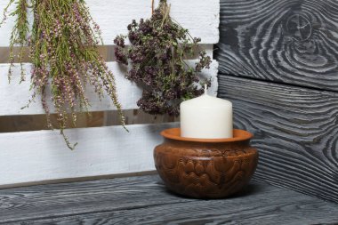 Kil bir kapta büyük bir mum. Yakınlarda bir sürü güzel kokulu bitki asılı. Siyah beyaz boyanmış tahtalarda duruyor..