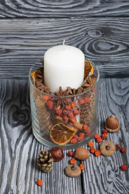 Cam bir kapta büyük bir mum. Koniler, dağ külleri, anason yıldızları, tarçın çubukları dekorasyon için içine dökülüyor. Meşe palamudu ve dağ külleri etrafa saçılmış. Boyalı tahtaların üzerinde durur