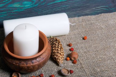 Kil bir kapta büyük bir mum. Meşe palamutları, Rowan çilekleri yakınlarda ve bir mum uzanıyor. Fırçalanmış tahtaların arka planına karşı.