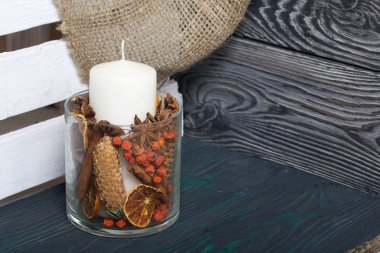 Cam bir kapta büyük bir mum. Koniler, dağ külleri, anason yıldızları, tarçın çubukları dekorasyon için içine dökülüyor. Dişlerimi fırçaladı.