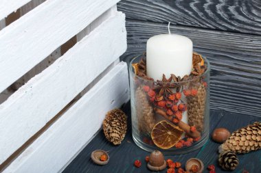 Cam bir kapta büyük bir mum. Koniler, dağ külleri, anason yıldızları, tarçın çubukları dekorasyon için içine dökülüyor. Meşe palamudu ve dağ külleri etrafa saçılmış. Boyalı tahtaların üzerinde durur
