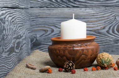 Kil bir kapta büyük bir mum. Meşe palamudu ve yaban mersini yakınlarda dağılmış. Fırçalanmış tahtaların arka planına karşı.