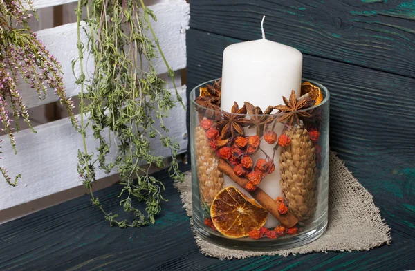 Cam bir kapta büyük bir mum. Koniler, dağ külleri, anason yıldızları, tarçın çubukları dekorasyon için içine dökülüyor. Yakınlarda bir sürü güzel kokulu bitki asılı. Boyanmış tahtaların üzerinde duruyor.