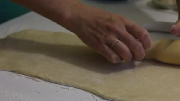 Žena válí těsto pro skořicové bonbóny. Stůl je posypaný moukou. Nedaleko je kontejner s buchtami na pečení. — Stock video