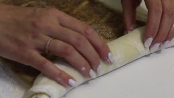 Kobieta roluje ciasto na bułkę cynobrową. Ciasto jest zwijane na powierzchni stołu. Posypane warstwą cynamonu z cukrem. — Wideo stockowe