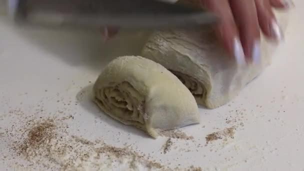 A woman cuts with a knife rolled into a roll dough for cinnabons. Nearby are cooking tools. Close-up shot. — Stock Video