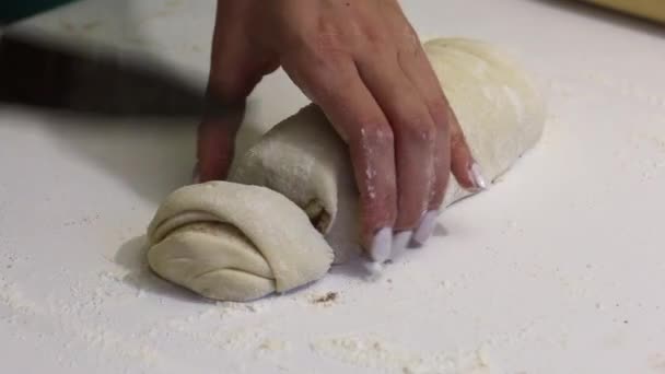 A woman cuts with a knife rolled into a roll dough for cinnabons. Nearby are cooking tools. — 비디오