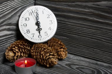 Fırçalanmış tahtalarda bir saat ve yanan bir mum. Yakında köknar kozalakları ve yanmış kibritler var..