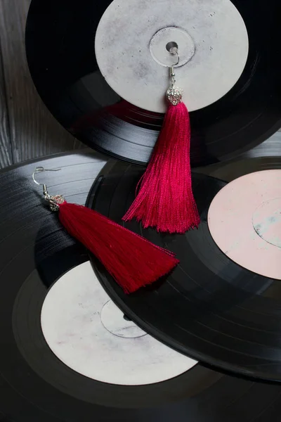 Pendientes de borla caseros en rojo. Sobre el fondo de viejos discos de vinilo y tableros de pino cepillado pintados en blanco y negro . — Foto de Stock