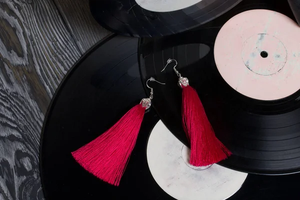 Pendientes de borla caseros en rojo. Sobre el fondo de viejos discos de vinilo y tableros de pino cepillado pintados en blanco y negro . — Foto de Stock