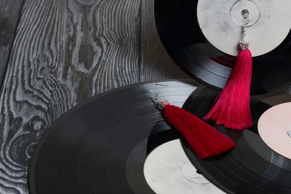 Pendientes de borla caseros en rojo. Sobre el fondo de viejos discos de vinilo y tableros de pino cepillado pintados en blanco y negro . — Foto de Stock