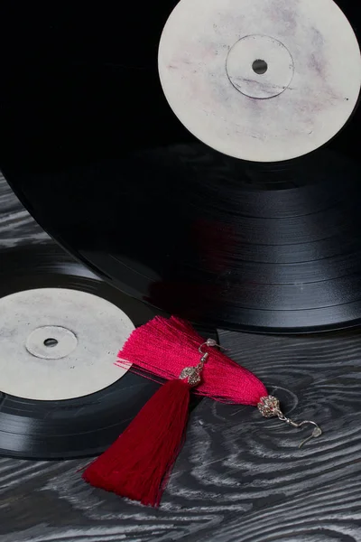 Brincos caseiros de borla em vermelho. Contra o fundo de discos de vinil antigos e placas de pinheiro escovado pintado em preto e branco . — Fotografia de Stock