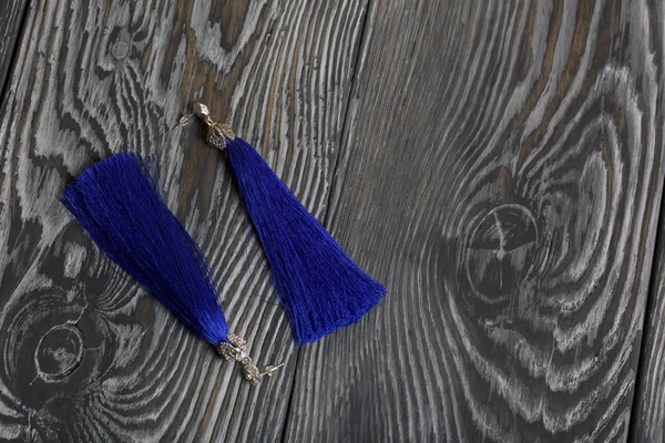 Pendientes de borla caseros en azul. Se tumban sobre tablas de pino cepillado pintadas en blanco y negro . —  Fotos de Stock