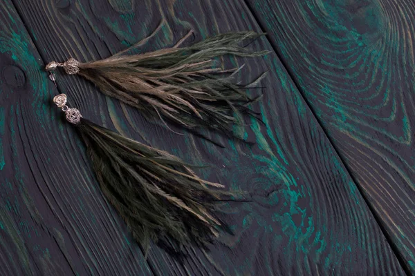 Orecchini in piuma di struzzo fatti in casa. Su tavole di pino spazzolato dipinte in nero e verde . — Foto Stock